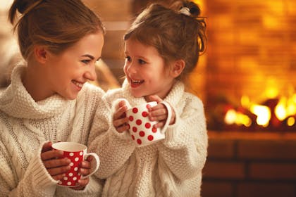Mum and daughter drinking from mugs in front of fire
