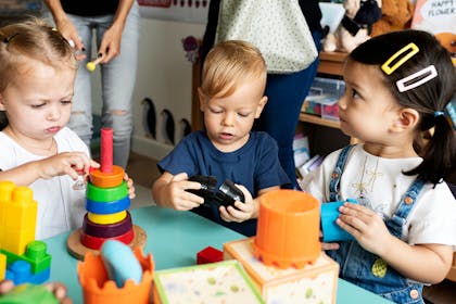 Three toddlers playing with toys on a table