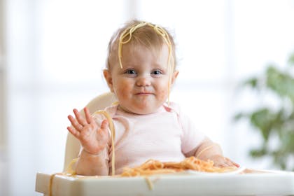 Smiling baby in highchair covered in spaghetti