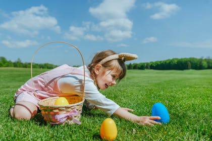 Little girl reaches for blue plastic egg hidden in grass