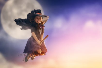 A young witch flies on a broomstick in front of the moon