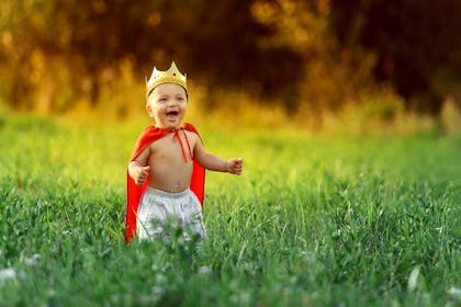 Toddler standing in a field of grass wearing a king costume