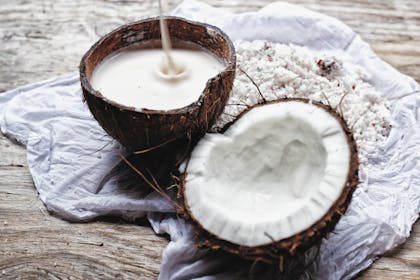 Two coconuts filled with coconut milk sat on a wooden table 