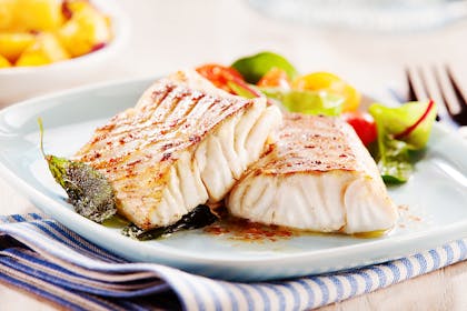 two fillets of cooked white fish on a plate with salad
