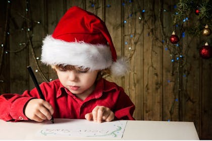 little boy in christmas hat writing