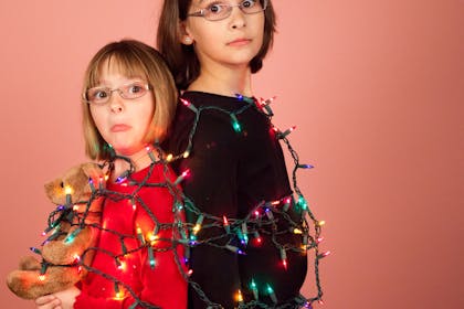 Two kids wrapped up in tangled Christmas tree lights