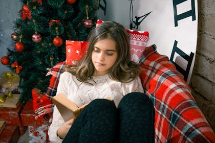 Girl snuggled up at Christmas reading a book