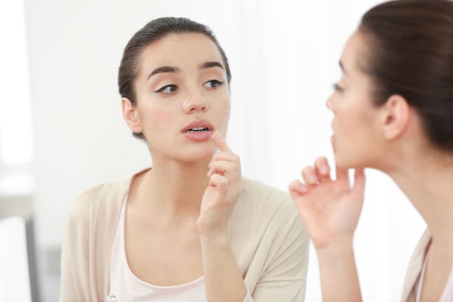 Woman putting cream on cold sore in mirror