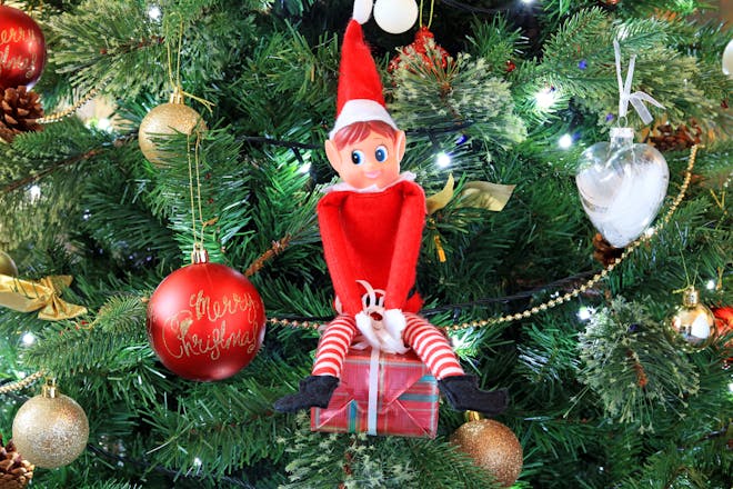 Elf on the shelf hiding in a Christmas tree with baubles and present decorations