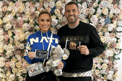 Man and woman hold up baby scans and teddy in front of flower wall