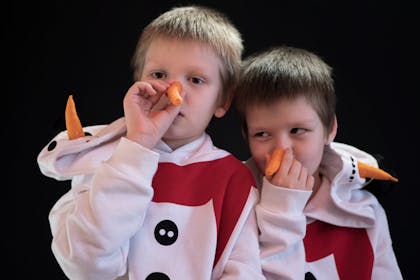 Two boys dressed in snowman costume hoodies holding carrots up to their noses
