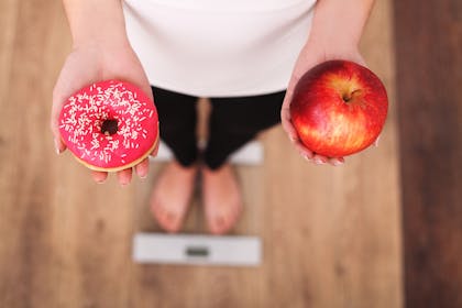 Woman on scales holding a donut and an apple