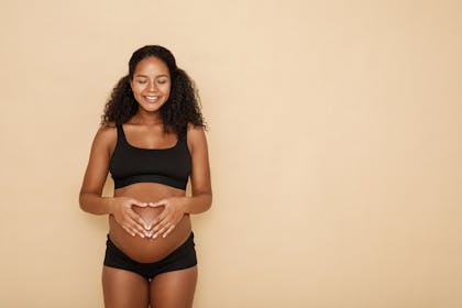 smiling pregnant woman making heart sign with her hands on her bump