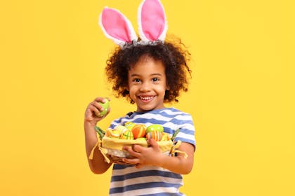 Child wearing bunny ears and holding an Easter basket full of eggs