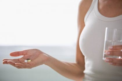 woman holding glass of water and tablets