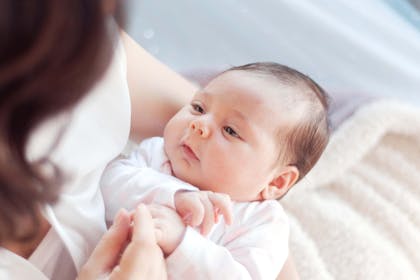 Baby held in mother's arms holding hands 