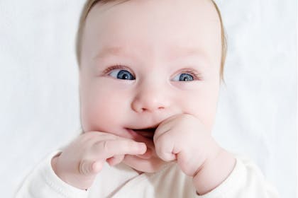Young baby smiling with fingers in their mouth