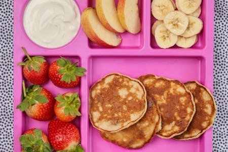 Pancakes on a pink tray with fruit and yoghurt