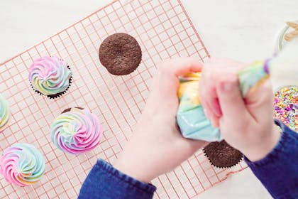 Person decorating cupcakes with multi-coloured icing