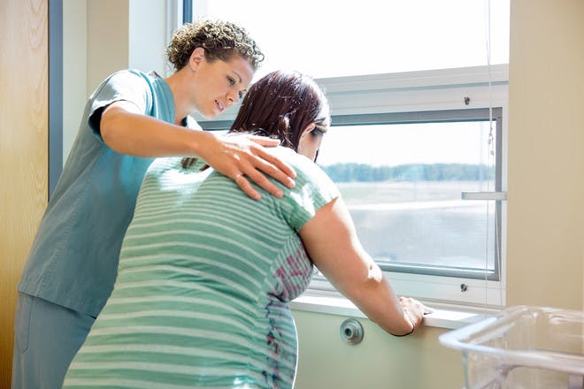 pregnant woman in labour in hospital leaning on window ledge with nurse comforting her
