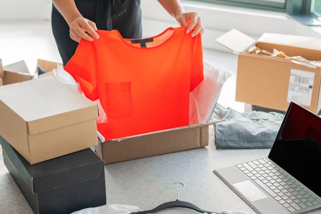 Woman pulling orange shirt from box after online shopping