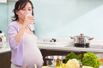 A pregnant woman drinking water and preparing vegetables
