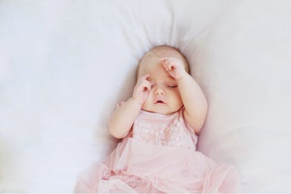 Baby girl wearing pink dress sleeping on bed 