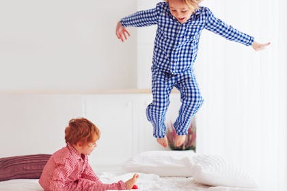 Two boys wearing checkered pyjamas and jumping on bed