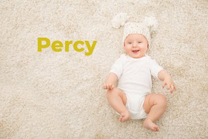 Baby lying on carpet with wooly hat on. Name Percy written in text