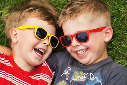 two brothers wearing sunglasses, lying on grass and laughing