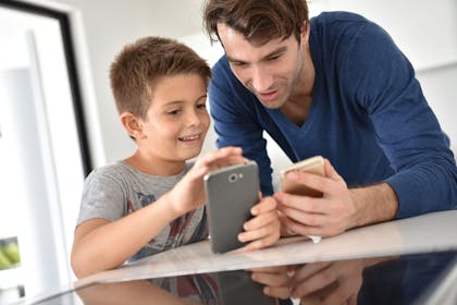Father and 7 year old son using smartphone together in kitchen
