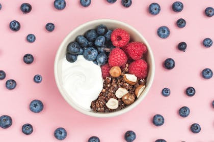Yoghurt in a bowl with berries, nuts and granola surrounded by blueberries