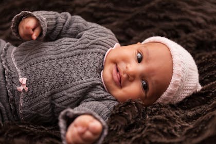 Smiling baby laying on their back wearing a knitted outfit and hat