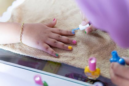 A child getting their fingernails painted in bright colours