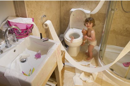 baby in messy bathroom with toilet roll everywhere