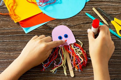 child making an octopus puppet with card, wool and an ice lolly stick