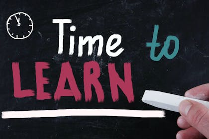 Hand and chalk written on a blackboard - 'Time to learn'.