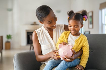 Young girl sitting on mum's knee holding piggy bank