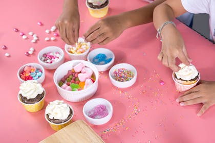 kids decorating cupcakes with bowls full of sweets and sprinkles