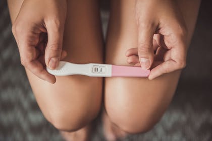 women sitting on toilet holding pregnancy test on her legs