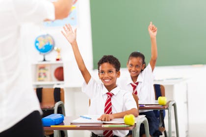 School children sitting at desks in class with their hands raised