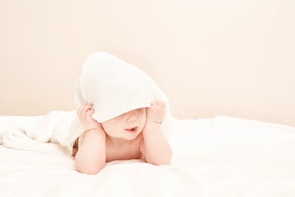 Baby hiding underneath white blanket 