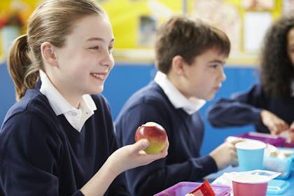 schoolgirl eating packed lunch and holding an apple