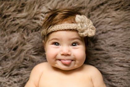 Cute baby smiling with tongue out and wearing a knitted flower headband