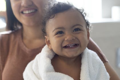 Smiling baby with curly dark brown hair and brown eyes wrapped in white towel