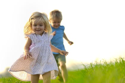 young girl and boy running outside in the grass