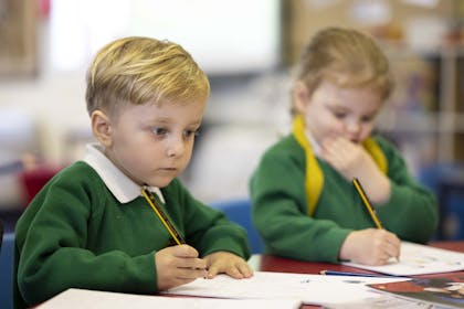 Young boy and girl in school uniform sitting at table and drawing with pencils