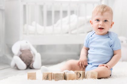 baby sitting up in his nursery next to building blocks
