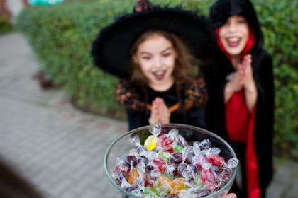 Two kids trick or treating with a bowl of sweets