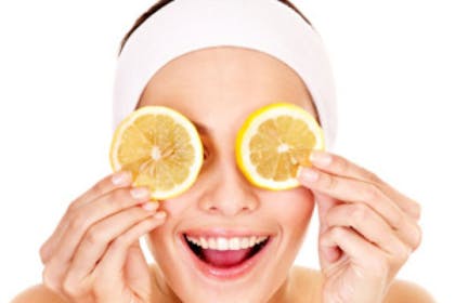 woman holding lemon slices to eyes